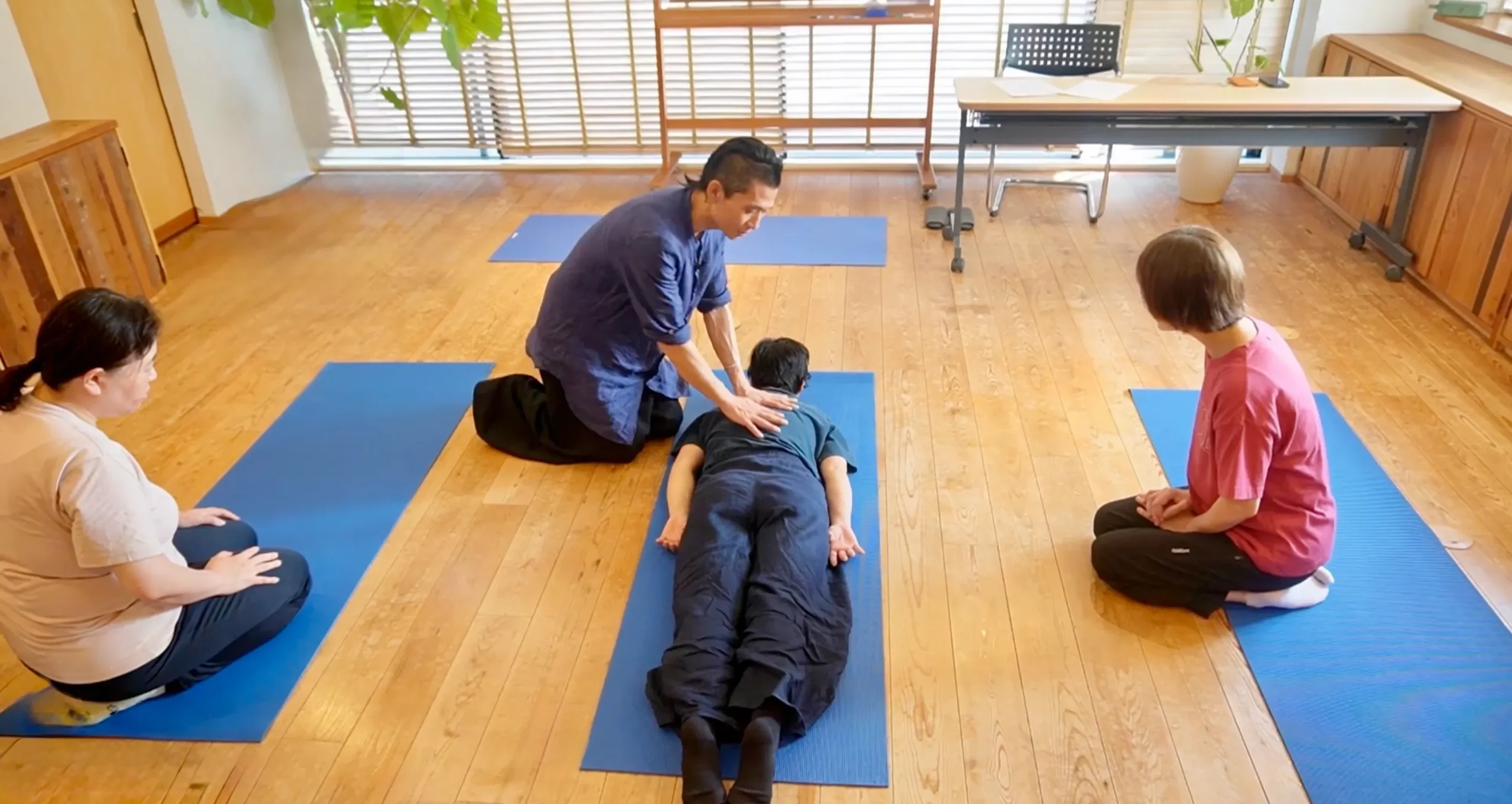 五十嵐靖が横たわる人に触れる実技を、周囲の参加者が見て学んでいる講座風景